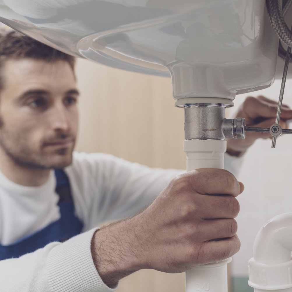 Professionele loodgieter die thuis een gootsteen repareert, hij controleert pijpen met een sleutel